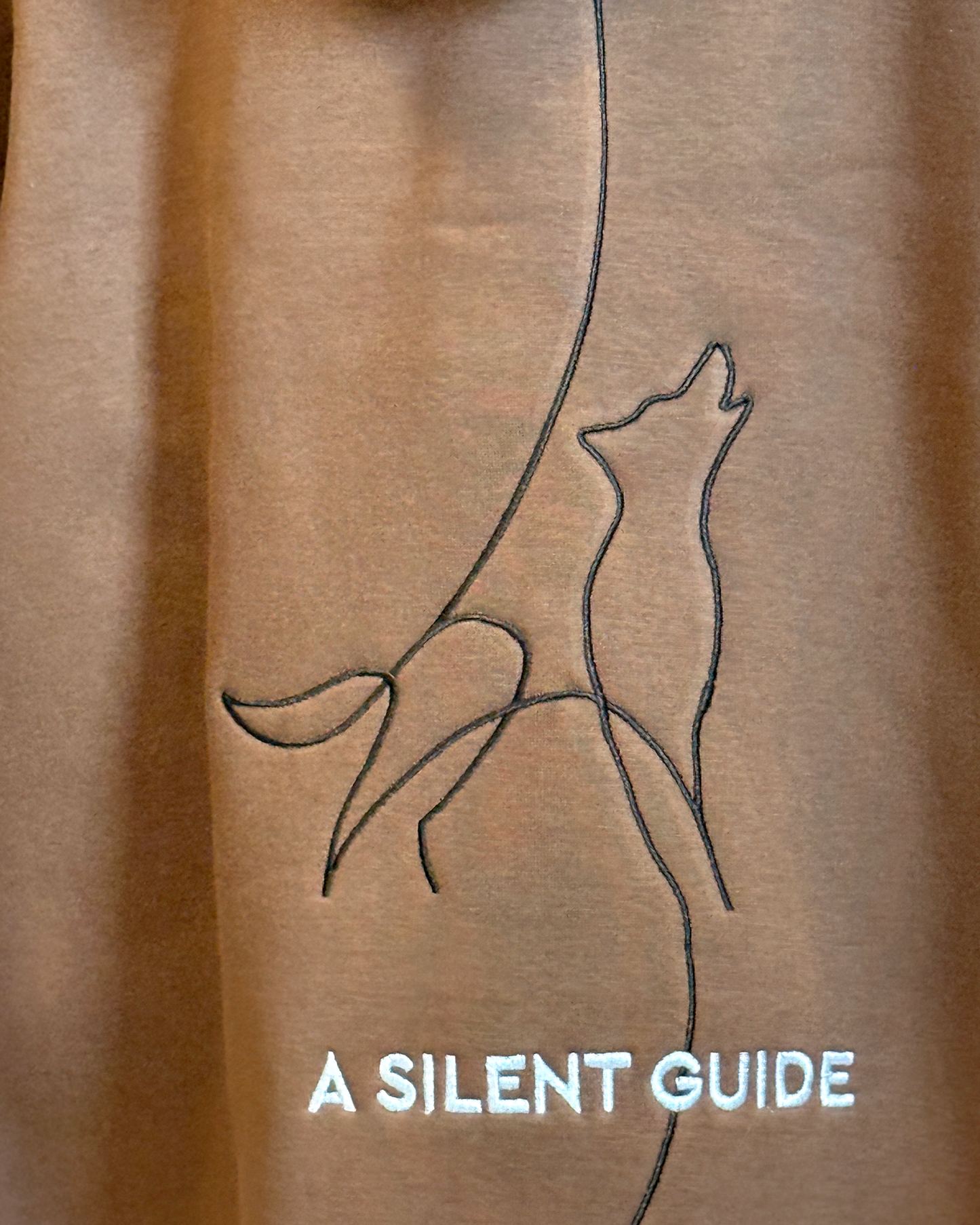 Zor Lifestyle, Brown Hoodie, Hoodies for men, Hoodies for Women, Brown hoodie with a line drawing of a wolf and 'A Silent Guide' text on a brown background